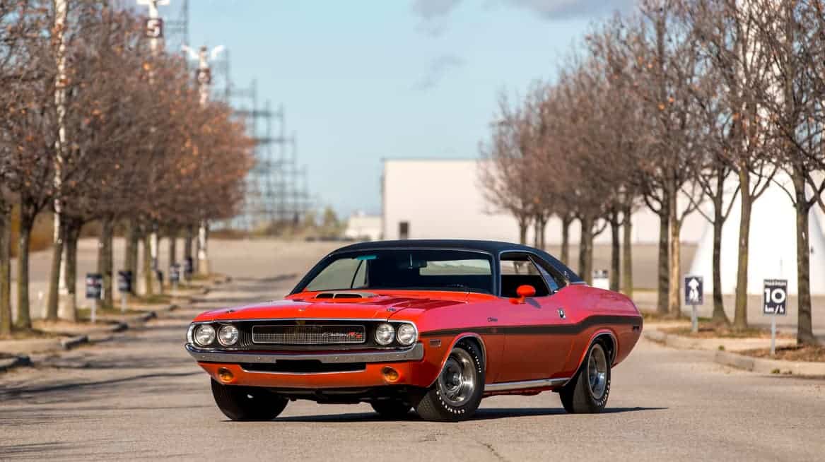 A restored 1970 Dodge Challenger R/T SE with a Hemi Orange exterior and black vinyl top. The car has a V-Code 440 Six Pack engine and dual exhaust with chrome tips.
